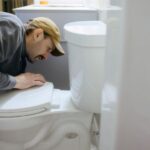 Person installing new toilet seat hinges with tools on bathroom floor