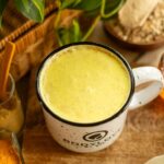 A warm, creamy mug of golden-colored ashwagandha milk, garnished with a cinnamon stick and star anise on a dark wooden table