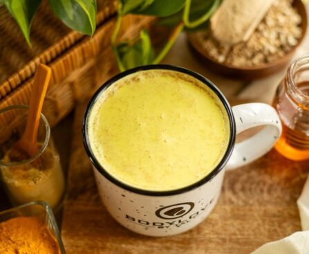 A warm, creamy mug of golden-colored ashwagandha milk, garnished with a cinnamon stick and star anise on a dark wooden table