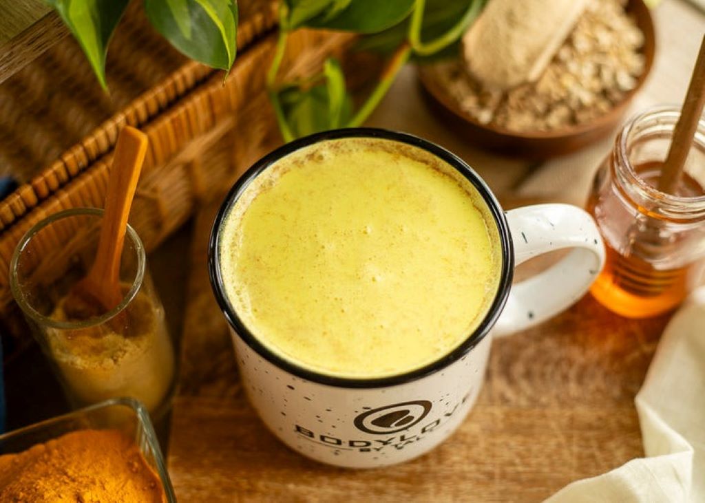 A warm, creamy mug of golden-colored ashwagandha milk, garnished with a cinnamon stick and star anise on a dark wooden table