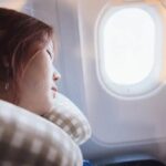 Woman sleeping peacefully on long flight using twisted Dot&Dot travel neck pillow against airplane window