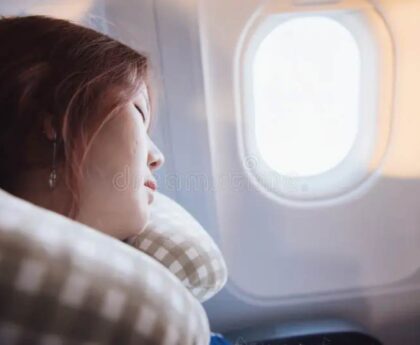 Woman sleeping peacefully on long flight using twisted Dot&Dot travel neck pillow against airplane window
