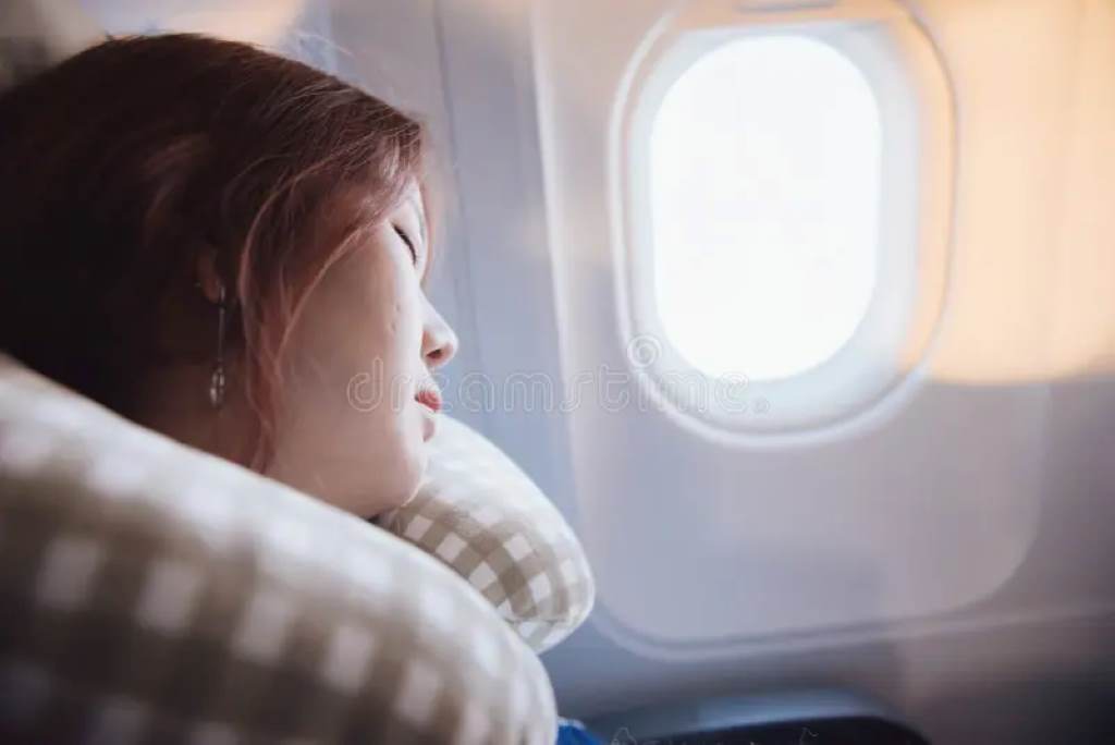 Woman sleeping peacefully on long flight using twisted Dot&Dot travel neck pillow against airplane window