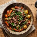 Steaming beef stew inside a stainless steel slow cooker on a kitchen counter.