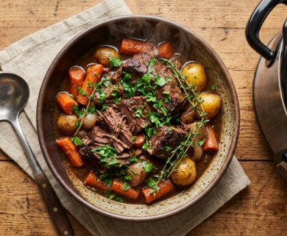 Steaming beef stew inside a stainless steel slow cooker on a kitchen counter.