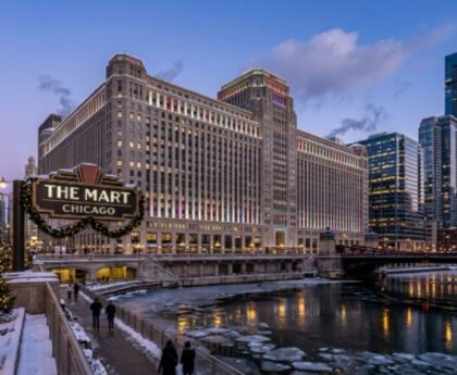 Exterior view of THE MART Chicago Art Deco building along the Chicago River during the winter holiday season with hotel towers visible nearby